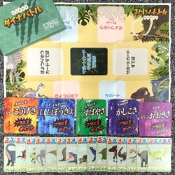 Dinosaur-themed board game setup with colored ability cards (Attack, Defense, Quick, Smart, Size) and a row of character cards at bottom.